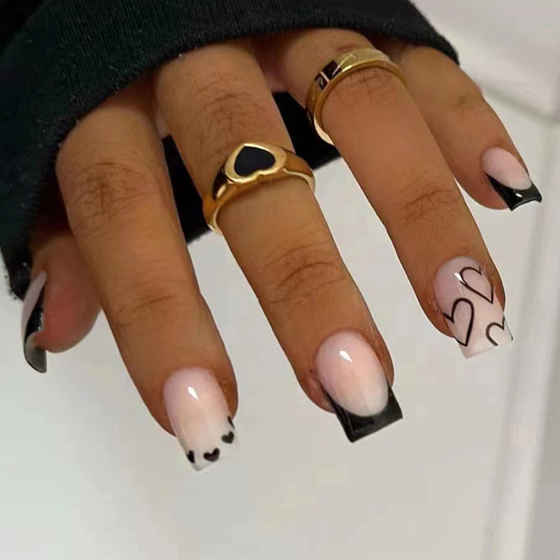 Hand with pink and black nail design wearing gold rings on a neutral background