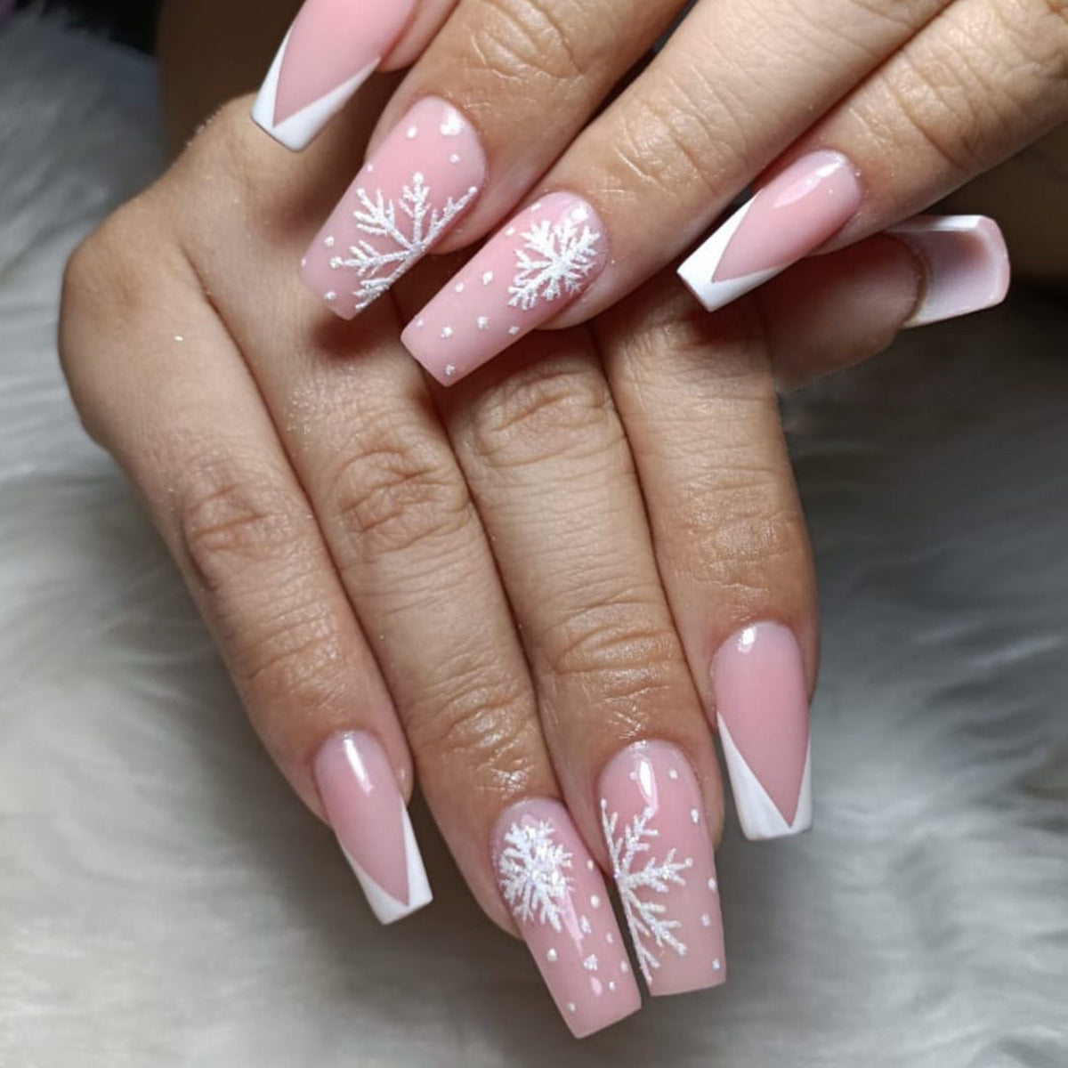 Close-up of a hand with pink nails featuring snowflake designs on a soft gray background.