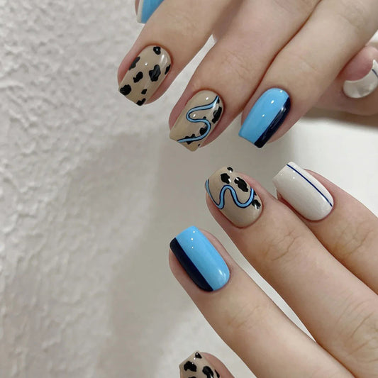 A set of short square press-on nails featuring blue hues and abstract patterns, including dots, lines, and animal-like figures.