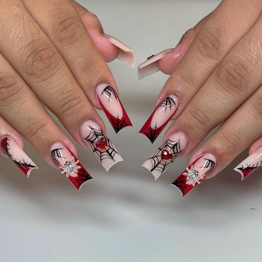 A set of long square press-on nails with red and pink spiderweb designs and rhinestone accents.