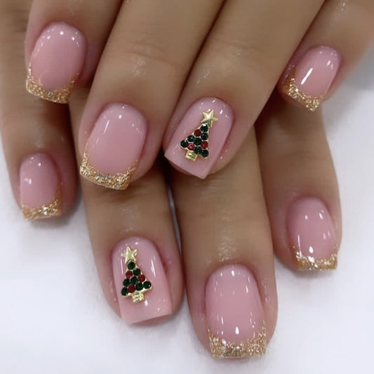 A set of press-on nails featuring a pink base with gold glitter and a Christmas tree design, displayed on a hand.