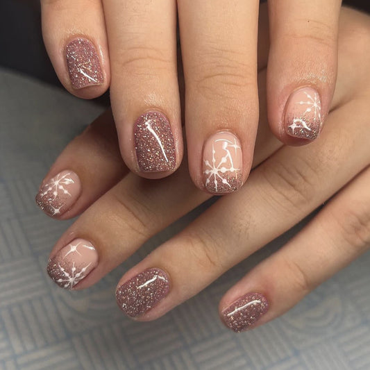 A set of press-on nails featuring a short square shape, adorned with a delicate snowflake design and rose gold glitter.