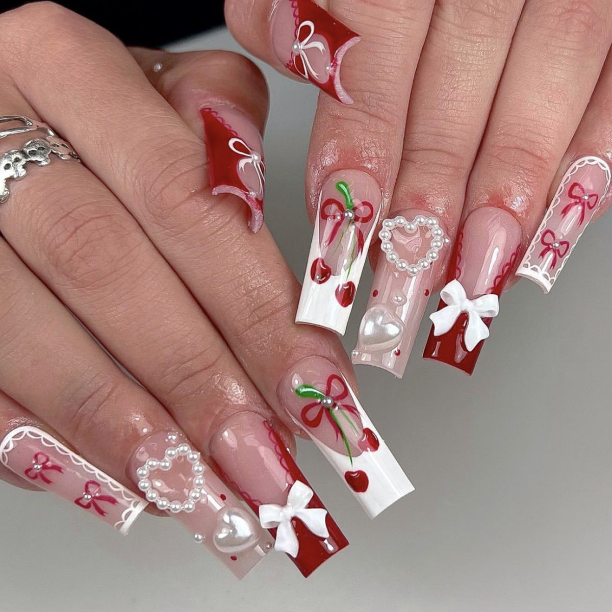 Nails with Valentine's Day-themed designs including hearts, bows, and cherries on a neutral background.