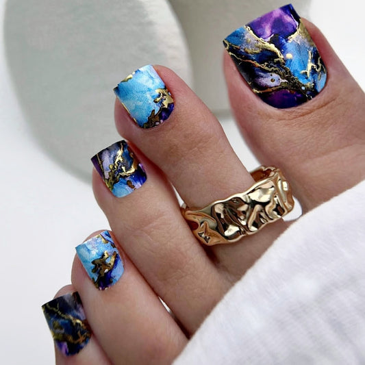 Hand with blue and gold marbled nail art wearing a gold ring on a white background