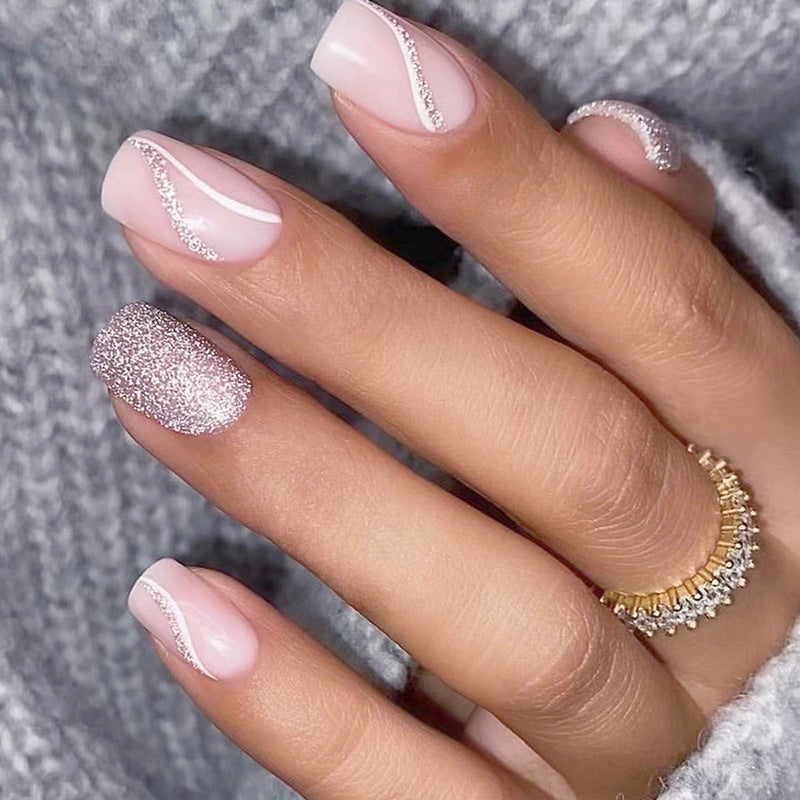 A set of pink press-on nails with glitter accents, displayed on a hand with a ring on the finger.