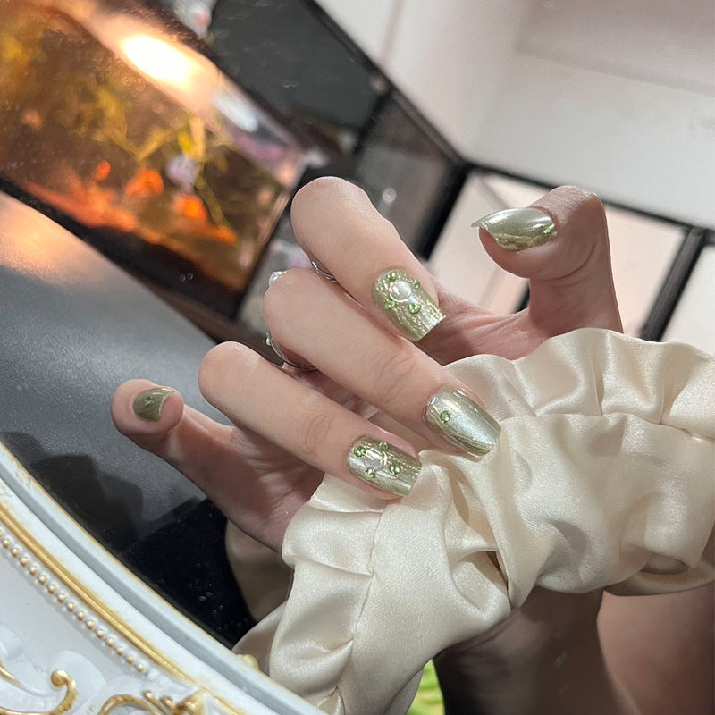 Hand with green nail polish wearing a white glove in front of a blurred background