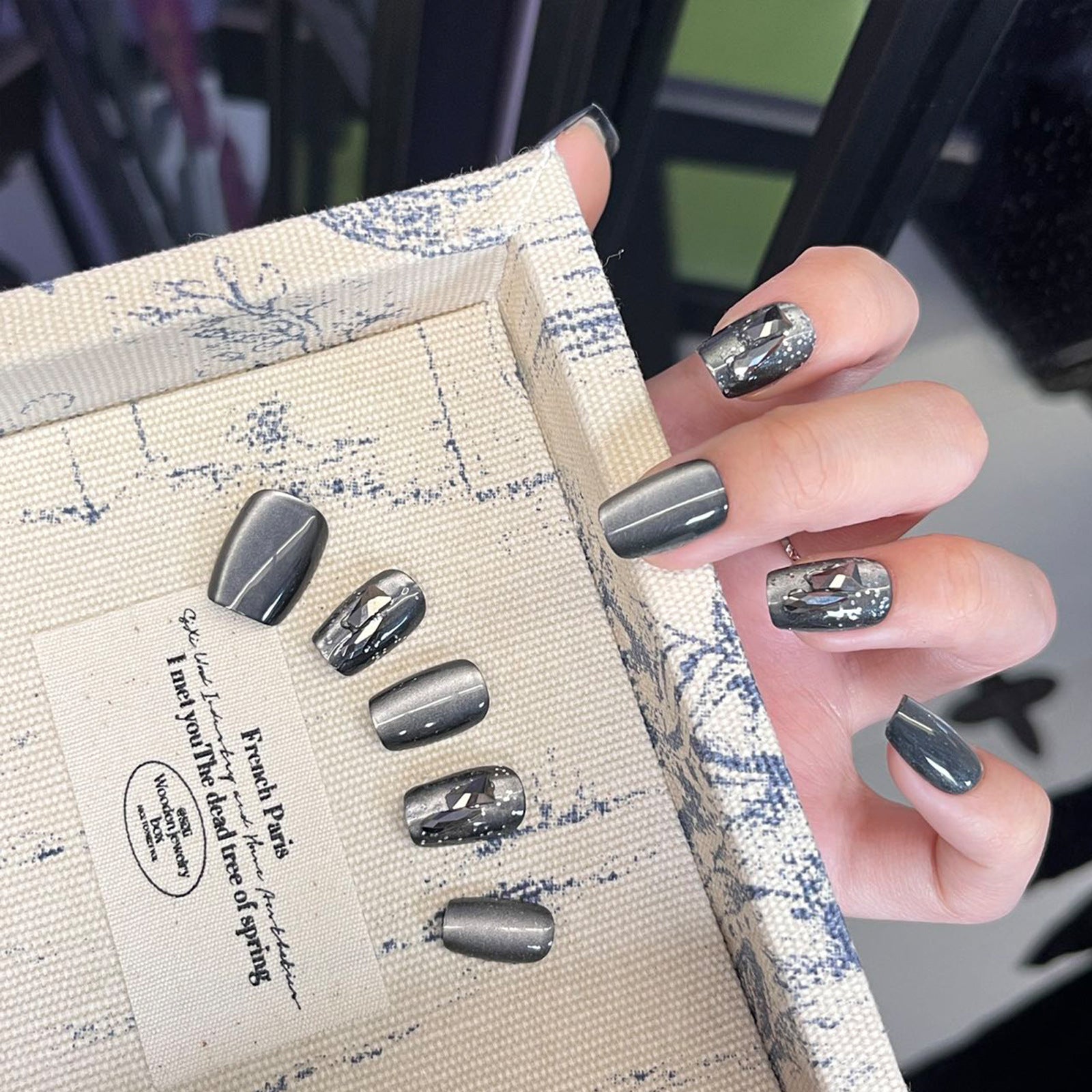 Nail art display with gray nail designs on a textured box