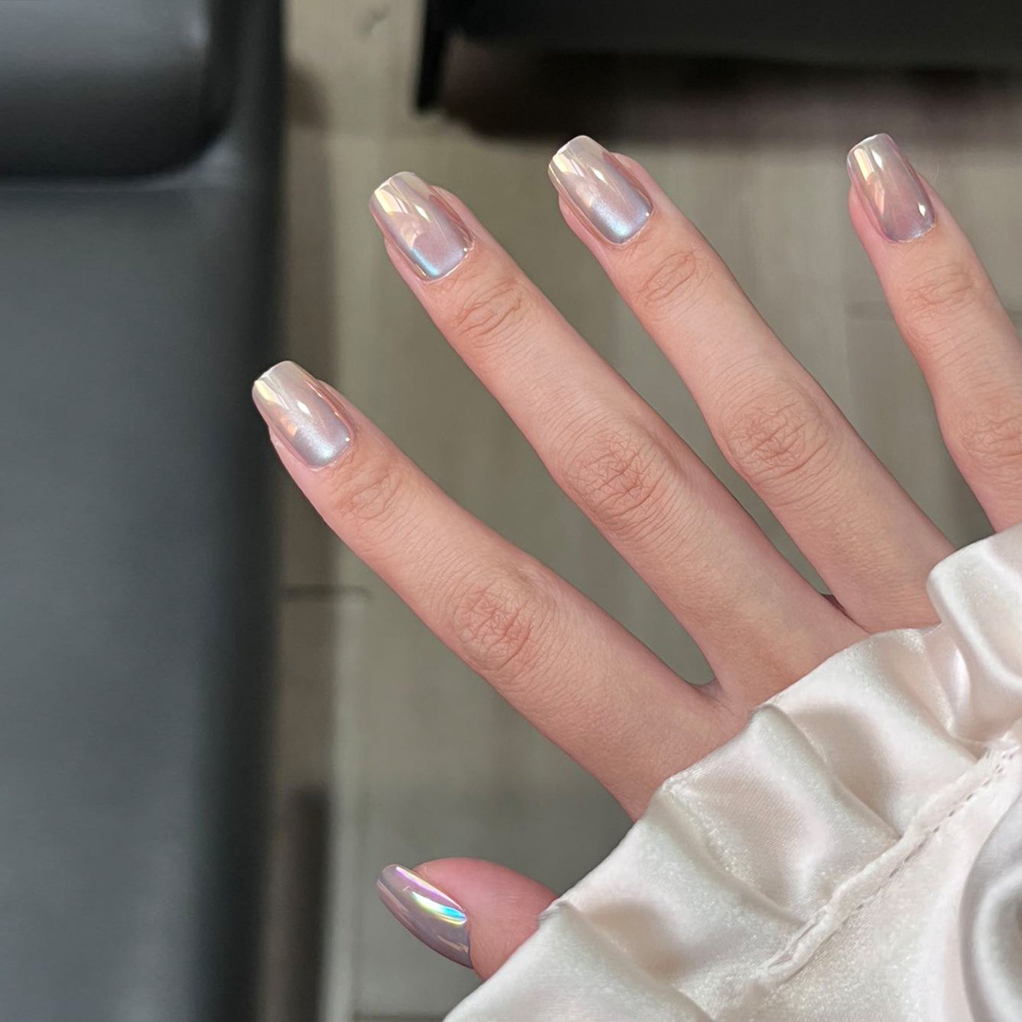 Close-up of a hand with iridescent nail polish against a neutral background