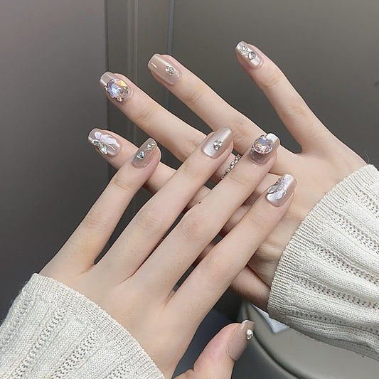 A set of press-on nails featuring a floral pattern with transparent and sparkling gem accents, presented on a pair of hands.