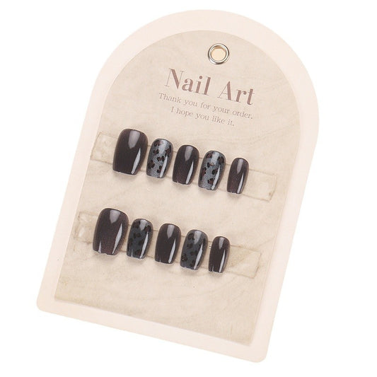 A set of glossy black press-on nails with leopard print accents, displayed in a card packaging.