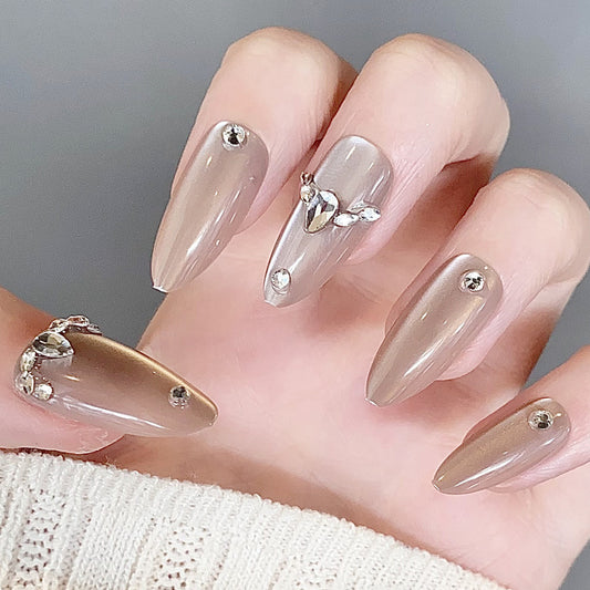 A set of beige almond-shaped press-on nails with rhinestone accents, shown with a shiny, glossy finish.