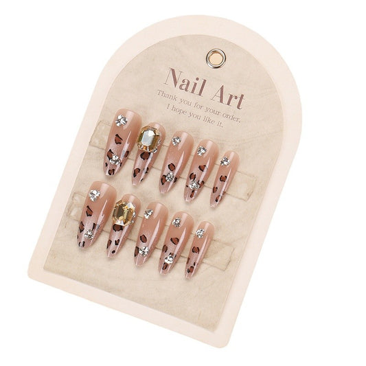 A set of beige almond-shaped press-on nails with sparkling rhinestones attached, displayed in a cardboard packaging with 'NAIL ART' written at the top.