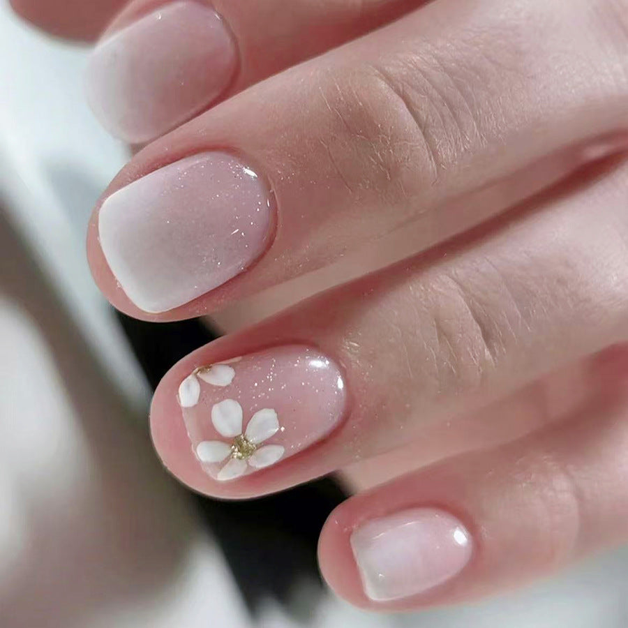 Close-up of a hand with pink nail polish and white floral design.