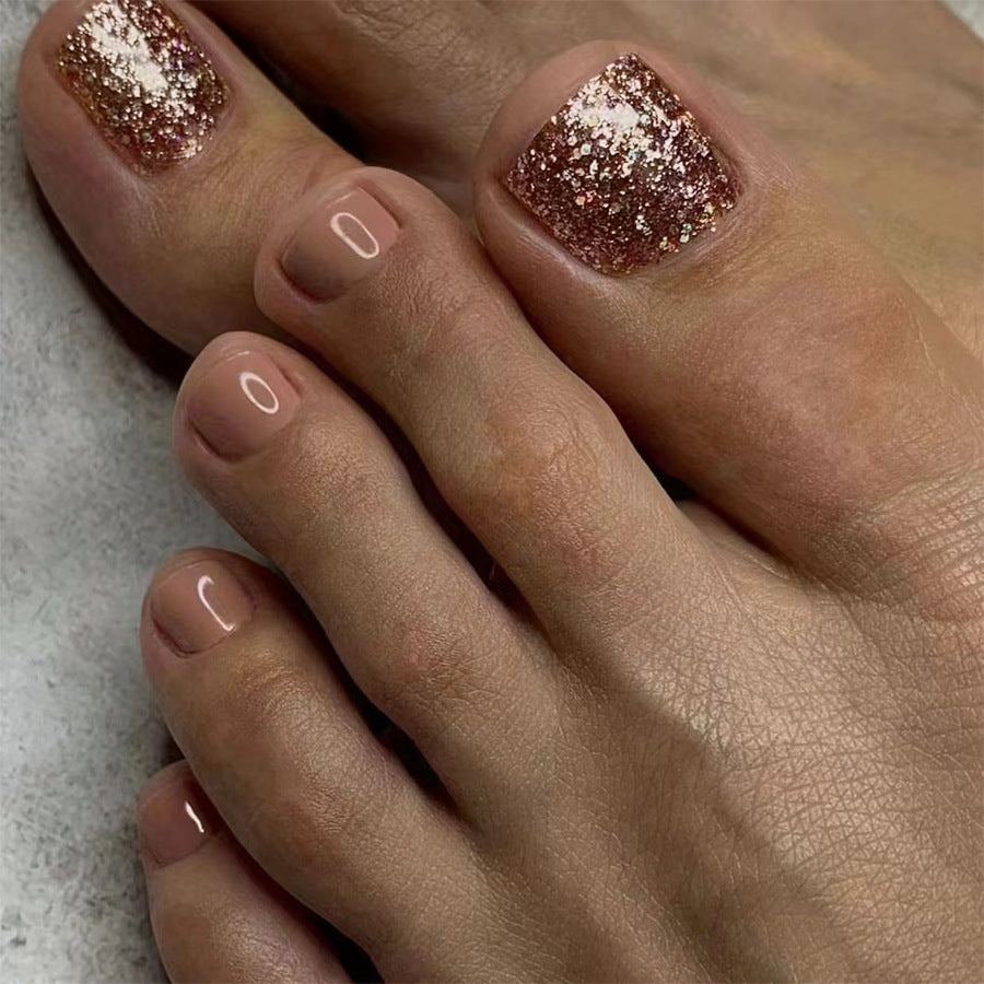 A close-up image of a person's feet wearing short square pink glitter accent press-on toenails.