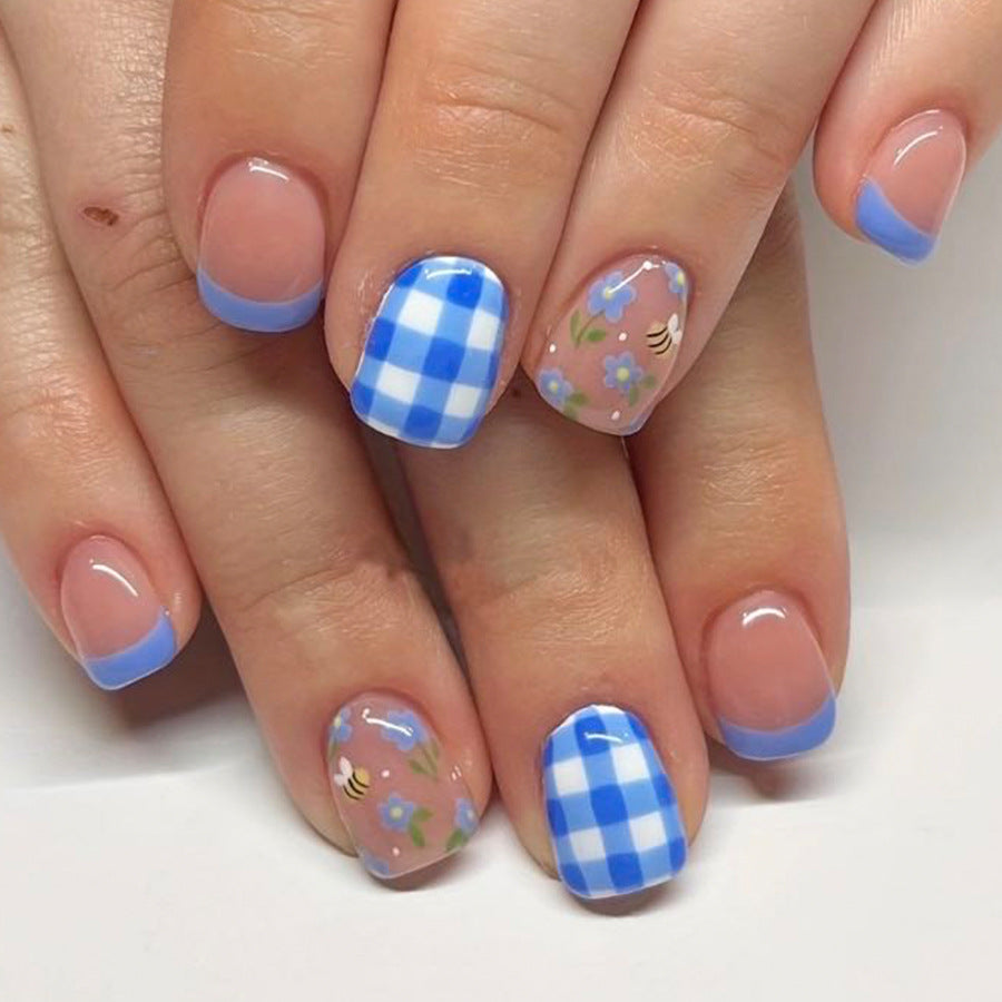 A set of press-on nails featuring a blue gingham and floral pattern, designed to resemble a spring picnic theme.