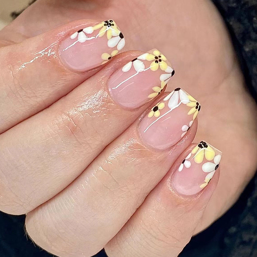 A set of beige press-on nails with floral detailing and yellow accents.