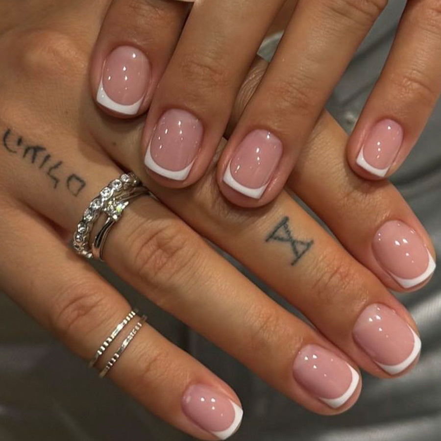 Close-up of hands with pink nail polish and tattoos on a neutral background
