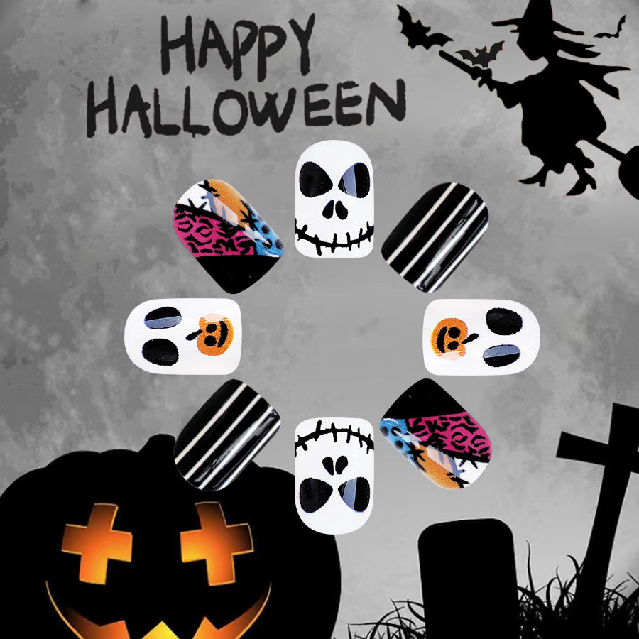 A set of multicolor press-on nails with skull and pumpkin designs, displayed against a Halloween-themed background with a witch and a pumpkin.