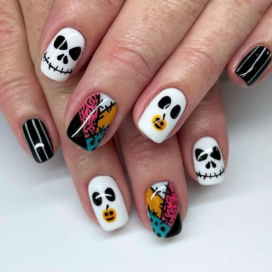 A set of press-on nails featuring a variety of designs including skeletons, pumpkins, and cats in black, white, and multicolor.
