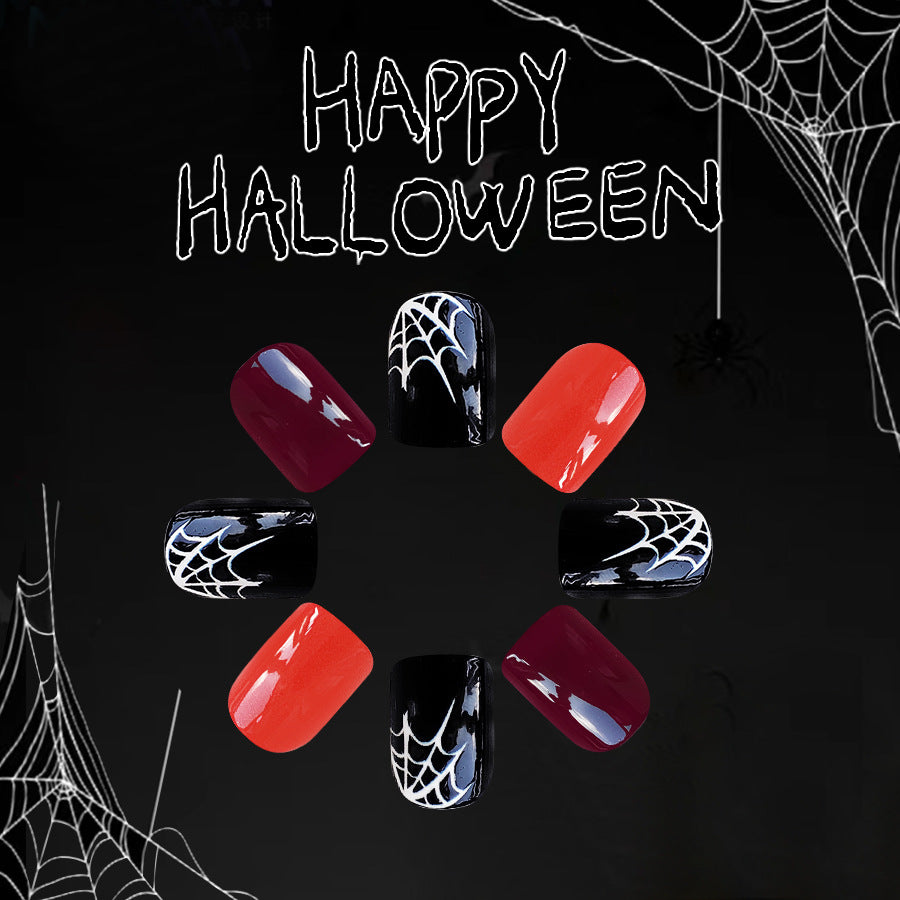 A set of press-on nails featuring a spiderweb design in black and red colors, displayed against a Halloween-themed background with spider webs and the text 'HAPPY HALLOWEEN'.