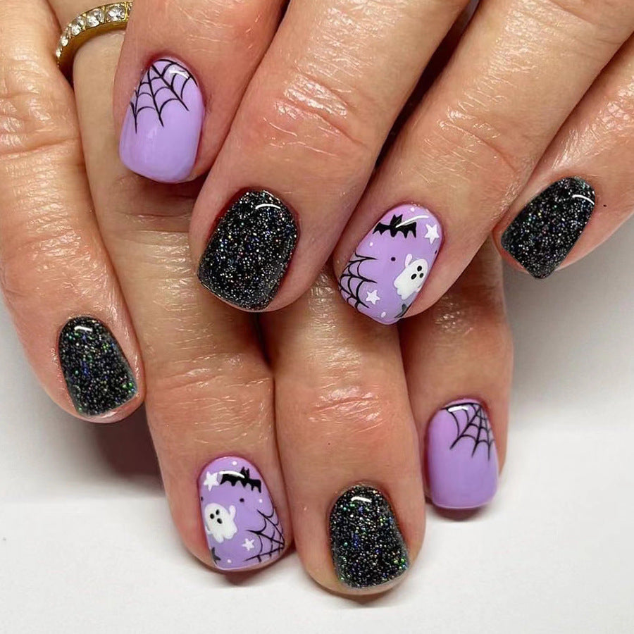 A set of press-on nails featuring a combination of purple, black, and glittery black colors with Halloween-themed designs including bats, pumpkins, and ghosts.