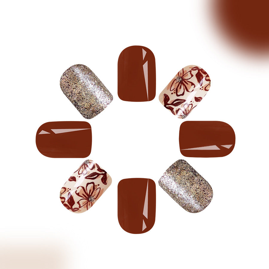 A set of press-on nails featuring a short square shape with a brown floral glitter design.