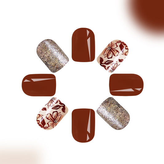 A set of press-on nails featuring a short square shape with a brown floral glitter design.