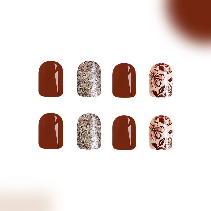 A set of four press-on nails featuring a mix of deep brown and gold glitter, with floral accents on the deep brown nails.