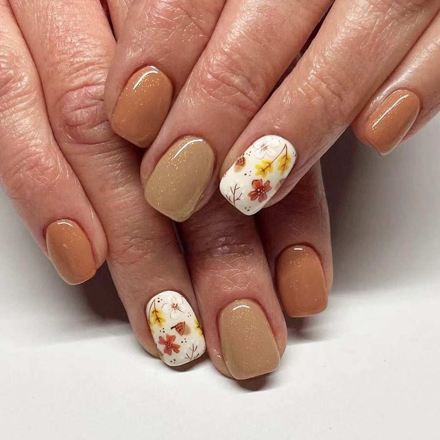 A set of beige and brown press-on nails with floral accents designed for short, square nails.