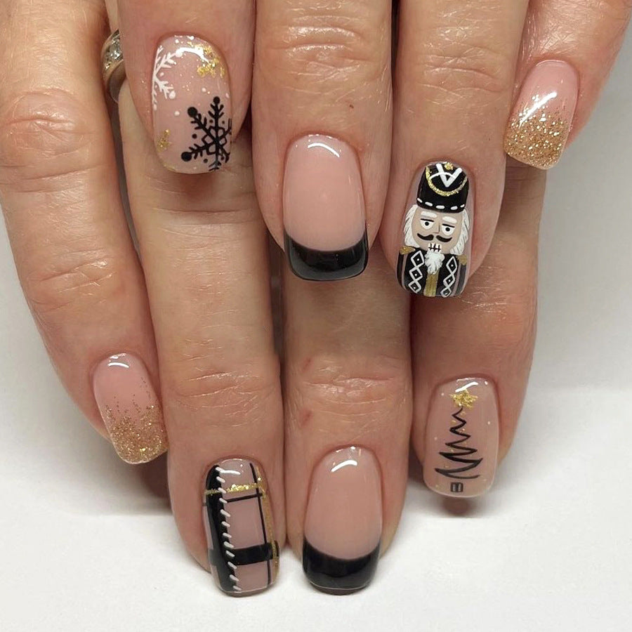 A set of press-on nail extensions featuring a variety of designs including a nutcracker, snowflakes, and other festive motifs in shades of pink, black, and gold.