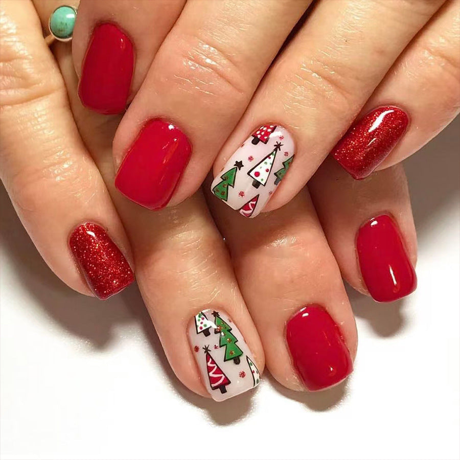 A set of press-on nails featuring a red base with Christmas-themed designs including a tree and ornaments, and the brand's logo.