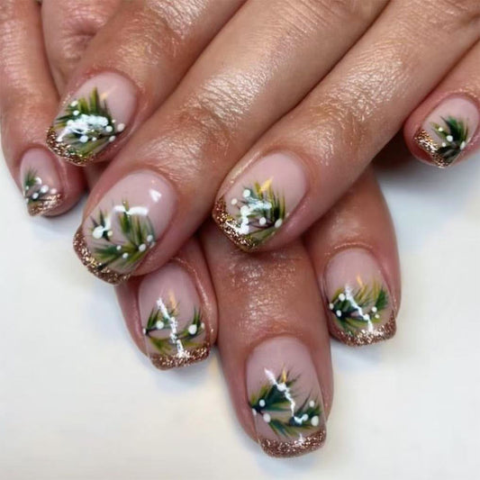 A set of press-on nails featuring an ombre design with green and white color gradient, adorned with small white and green floral patterns and a gold glittery finish.