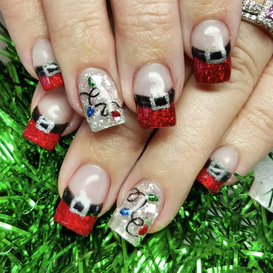A set of press-on nails featuring a red and glittery design with a Christmas-themed pattern, including a Santa belt, displayed on a hand against a green and red background.