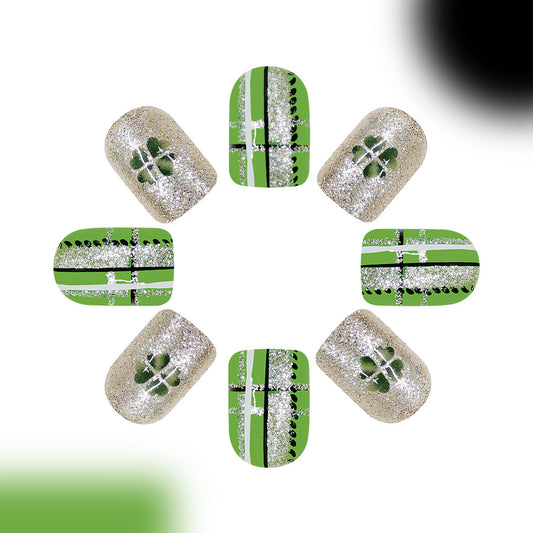 A set of false nails presented against a white background, featuring a short square shape with a green and silver shimmer design with unique cross patterns.