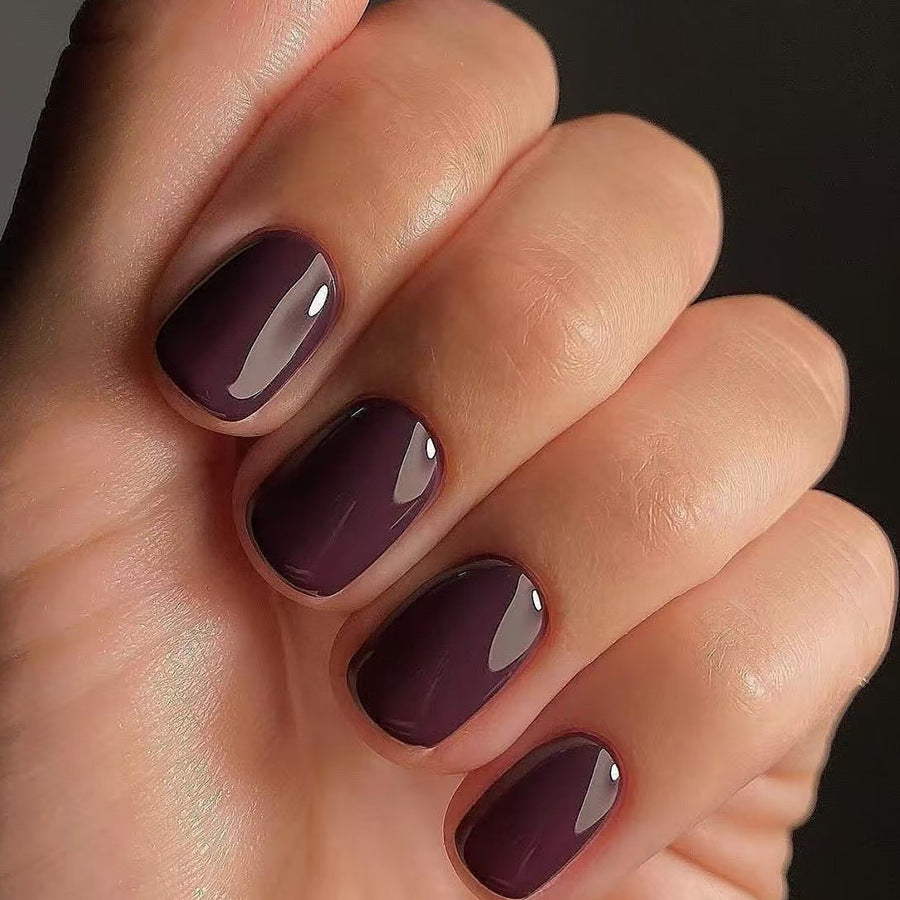 A close-up image of a person's hand showcasing short square-shaped nails with a deep purple glossy finish.
