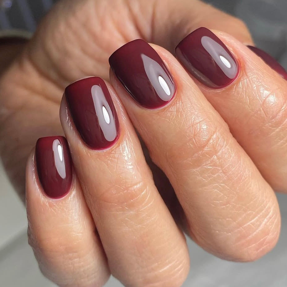 Close-up of a hand with burgundy nail polish on a neutral background
