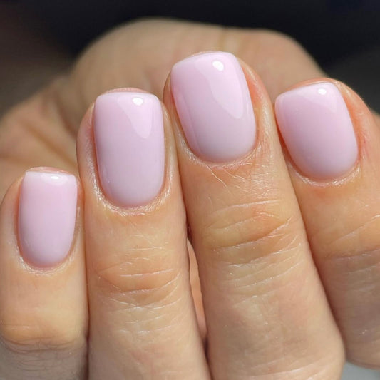 Close-up of a hand with light pink nail polish on a blurred background