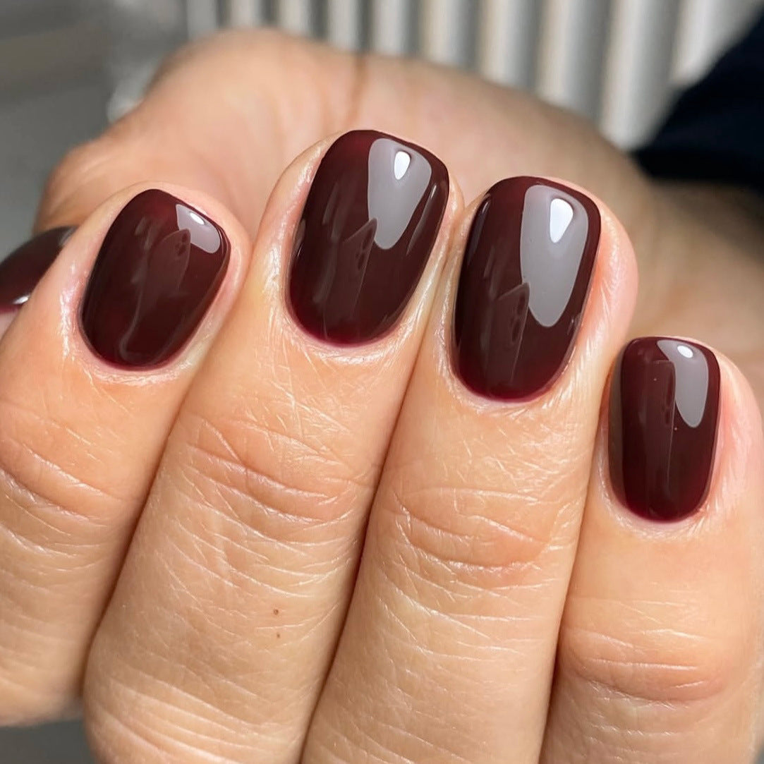 Close-up of a hand with dark red nail polish on a neutral background