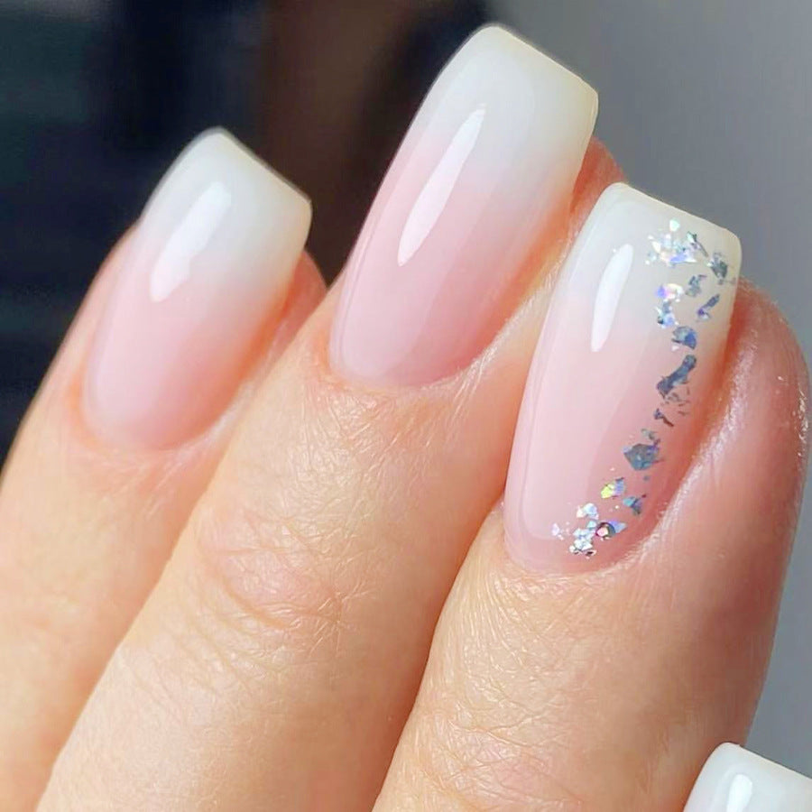 Close-up of a hand with white and pink gradient nails featuring small decorative elements.
