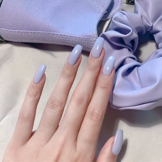 A pair of medium-sized, light purple, glossy finish press-on nails presented on a person's hand.