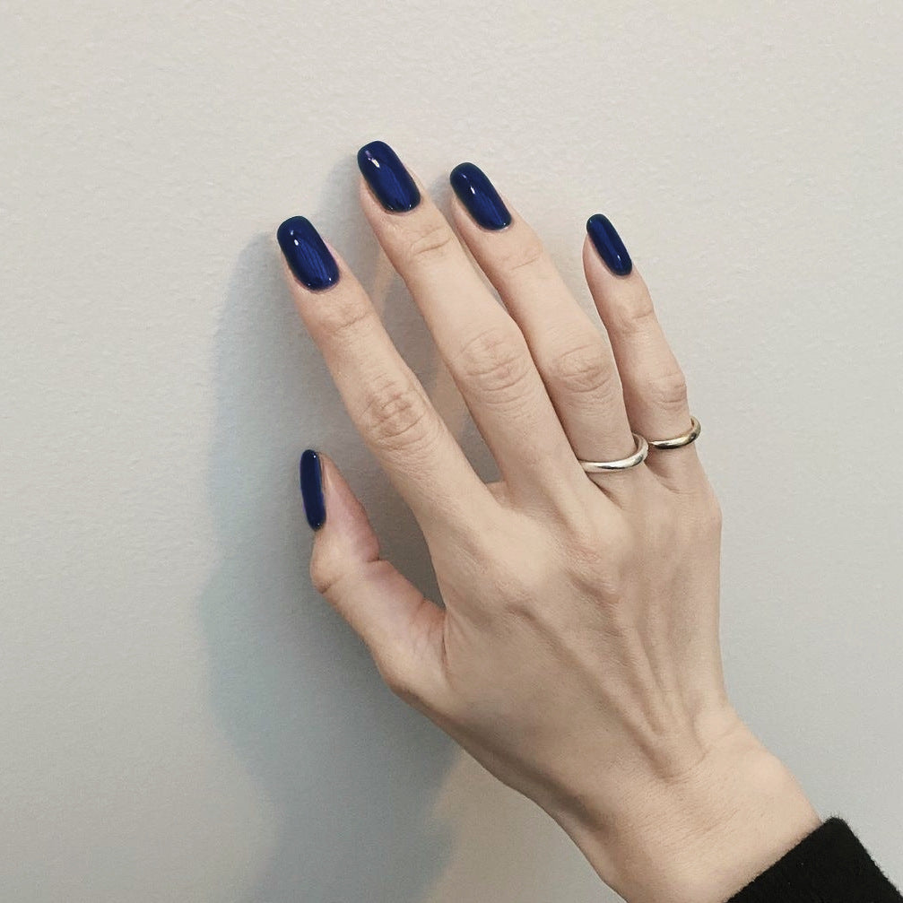 Hand with dark blue nail polish and two rings on a plain background