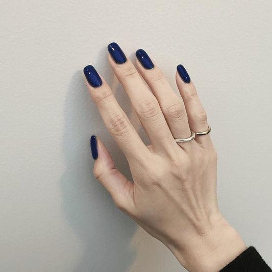 Hand with dark blue nail polish and two rings on a plain background