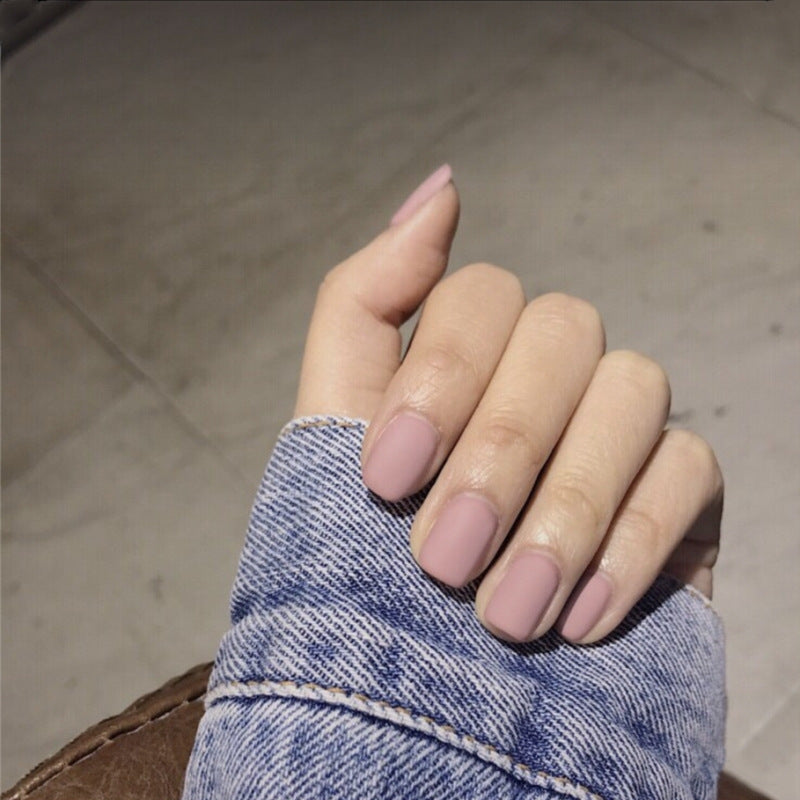 Hand with pink nail polish wearing a denim sleeve on a neutral background