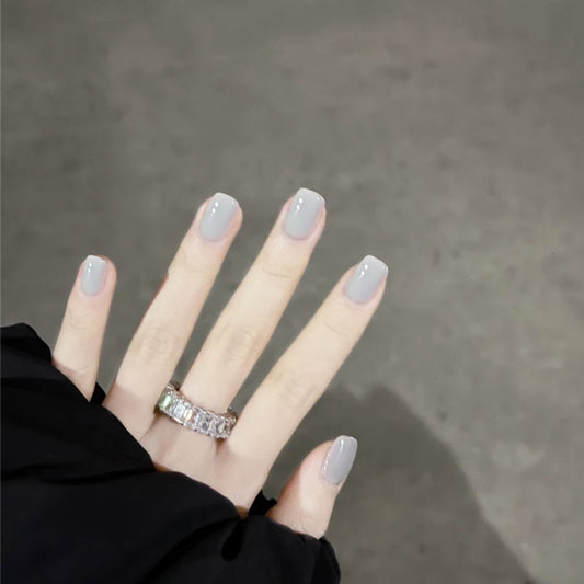 Hand with light gray nail polish and a ring on a neutral background