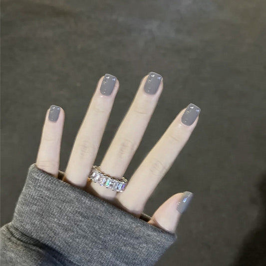 A hand with short square taupe nails with glitter accents, wearing a grey sweater.