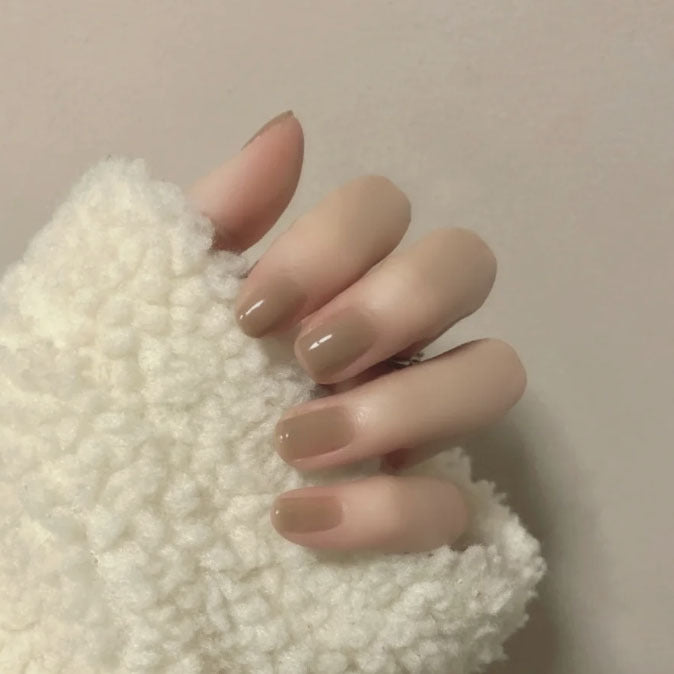 Hand with beige nail polish on a textured white surface