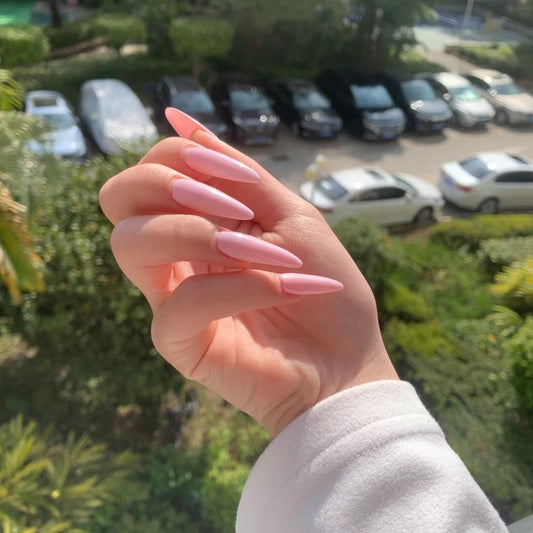 A hand with pink press-on nails displayed against a backdrop of cars in a parking lot.
