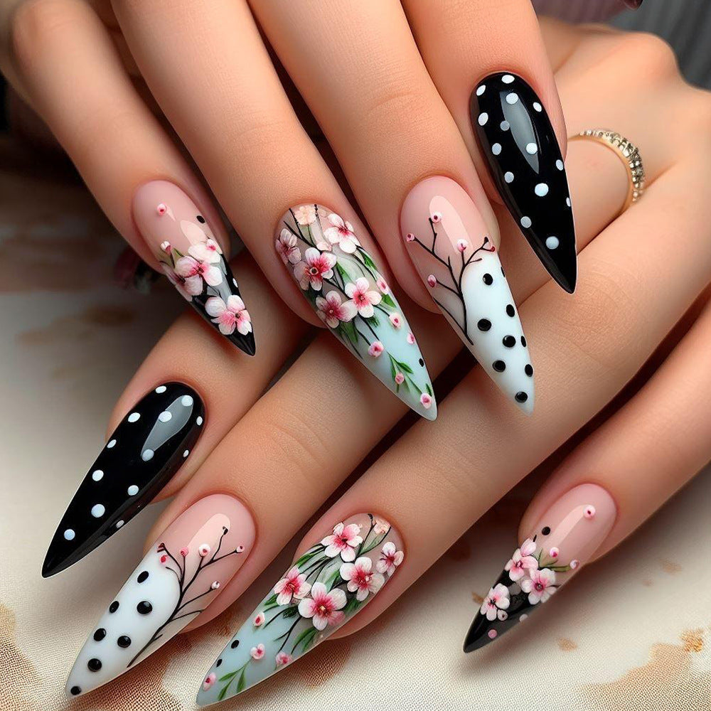 A set of press-on nails featuring a floral and polka dot design on a stiletto nail shape, with colors primarily in black, white, and various shades of pink.