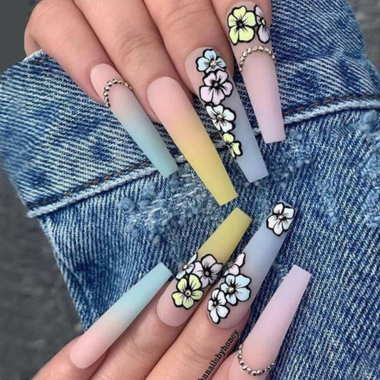 A set of long, gradient press-on nails with hand-painted floral designs in pastel colors.