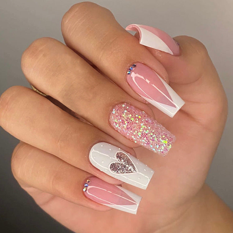 Hand with pink and white acrylic nails featuring heart and glitter designs.